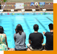 students sit by large swimming pool